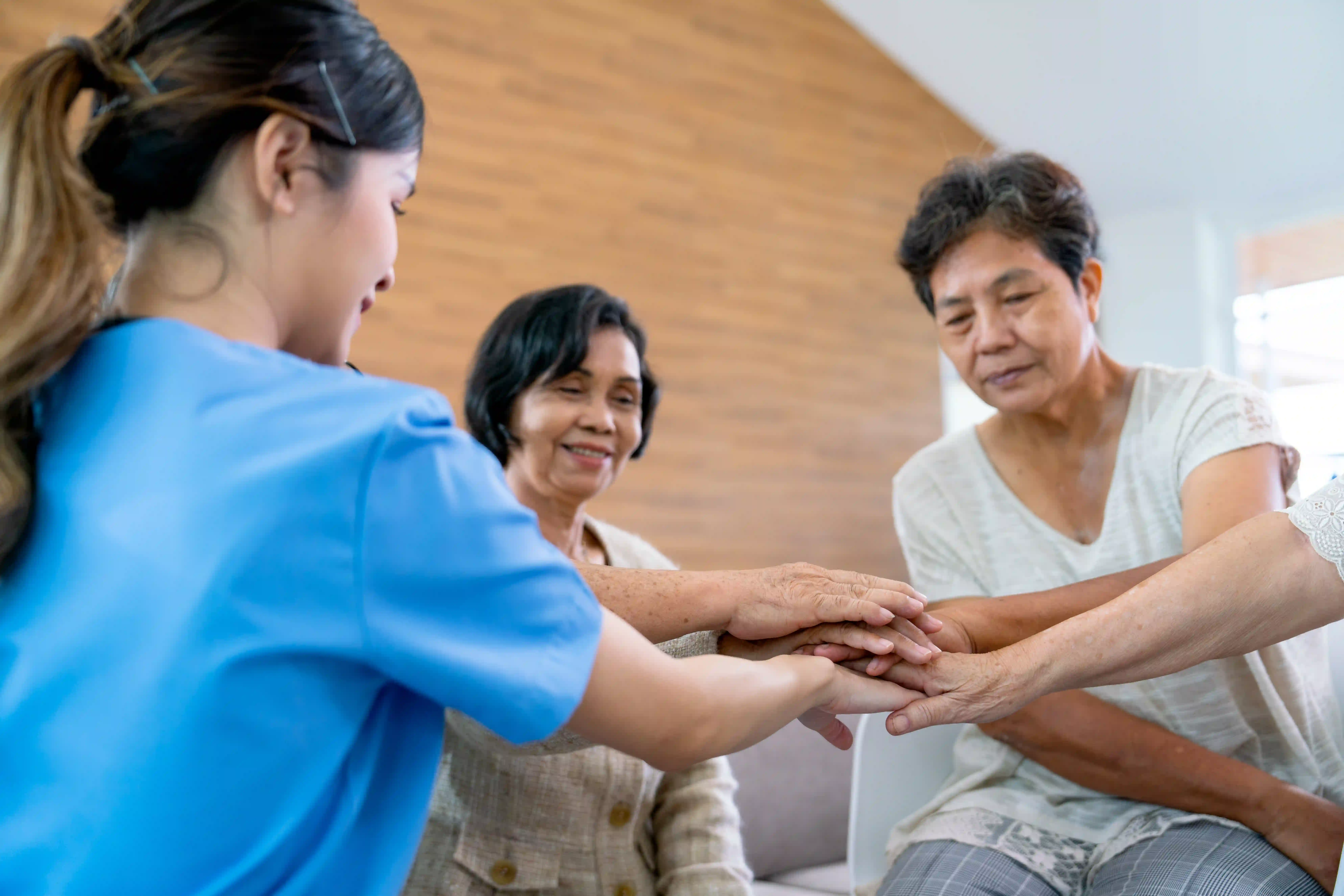 Caregiver joining hands with elderly group home residents